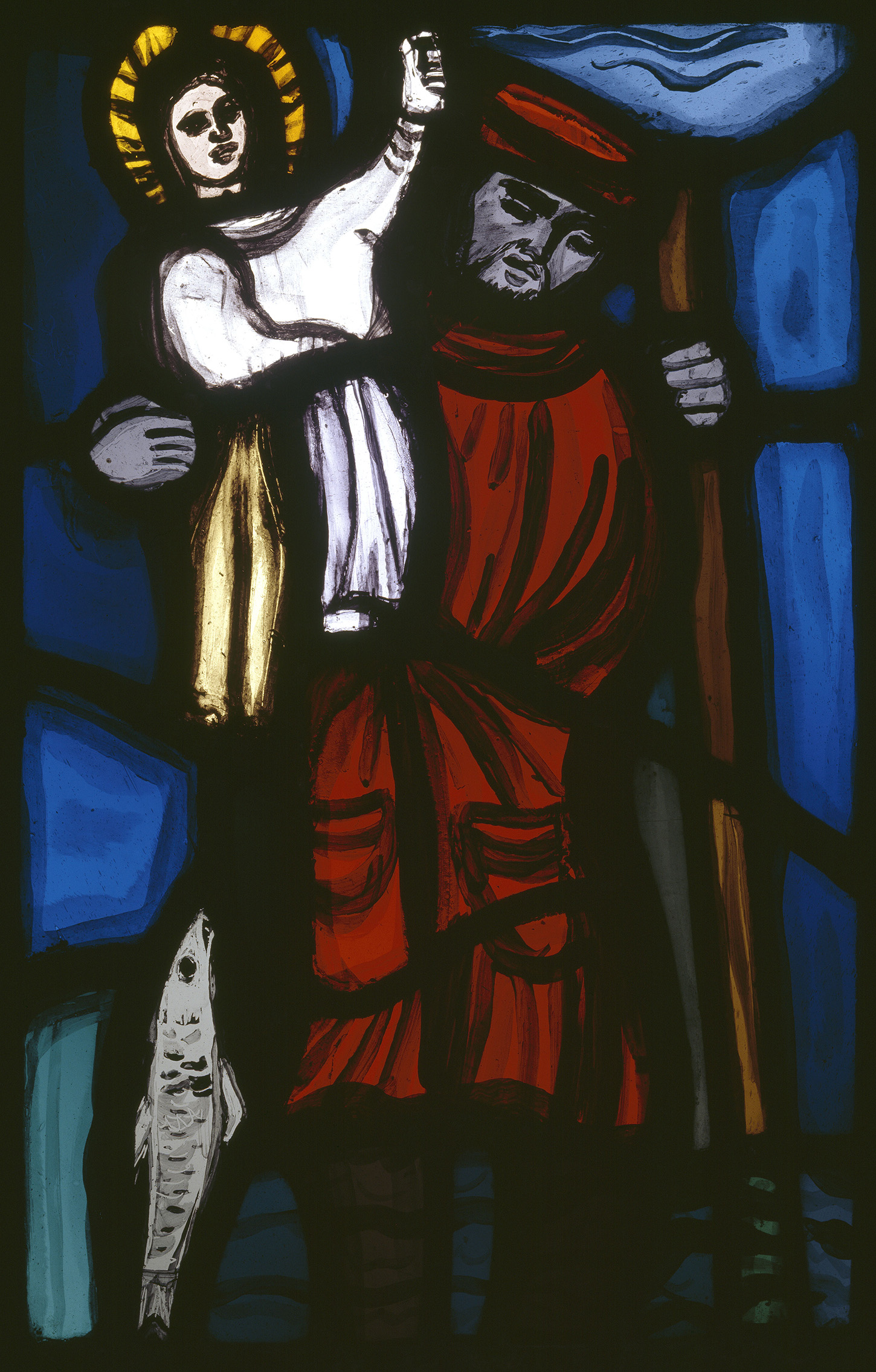 A stained glass work showing a figure in red, holding a staff, holding aloft a child in white, with a halo, who is raising a hand. At the bottom left of the glass is a fish.