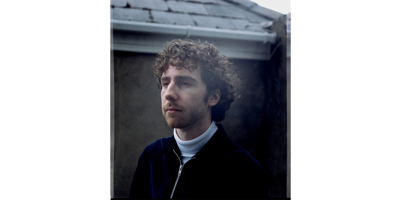 Portrait of a man with brown curly hair, wearing a dark blue velvet jacket