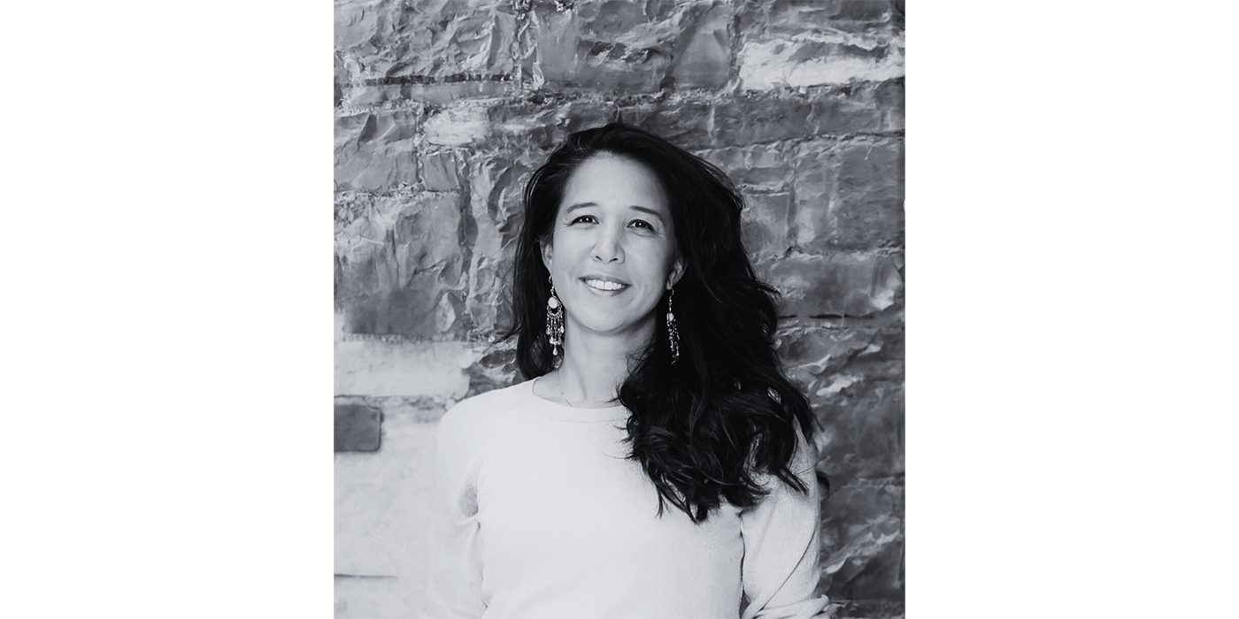 Black and white photograph of a woman with long dark hair, wearing a light coloured top and statement earrings