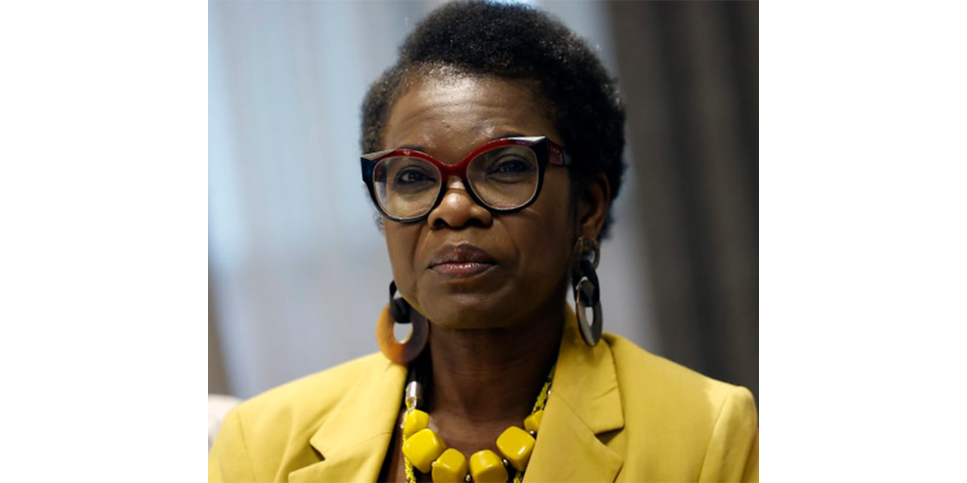 Headshot of a black woman wearing black glasses, a yellow jacket and a yellow sculptural necklace.