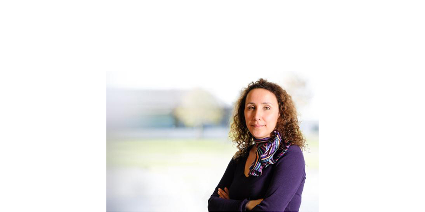 Headshot of a woman with brown curly hair against a blurred backdrop