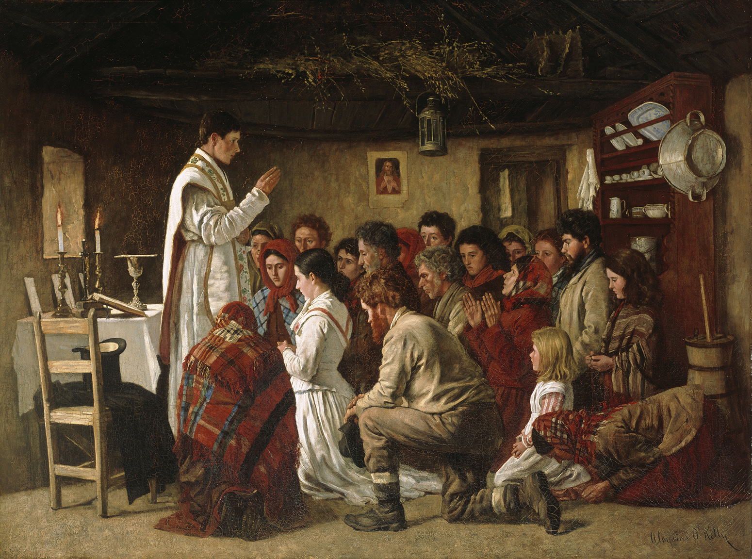 A priest stands in a cottage saying mass. Around him, people of all ages are kneeling.