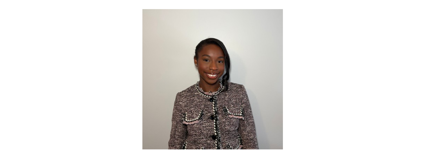 Headshot of a black woman wearing a grey tweed jacket, standing against a plain white wall