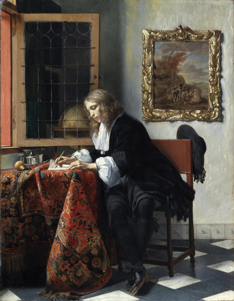 Detail of a man writing at a desk covered in a heavily patterned cloth.