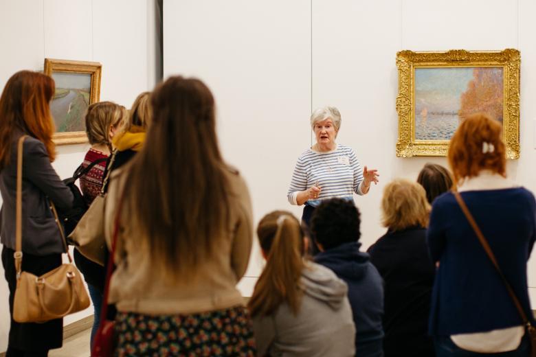 Tour guide speaking to a group in front of a painting by Monet