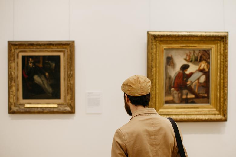 A man standing in front of two gilt-framed paintings in a gallery