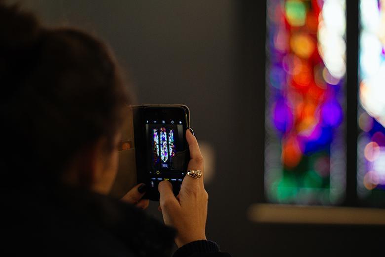 Photo of a woman using her phone to take a photo of stained glass in the National Gallery of Ireland.