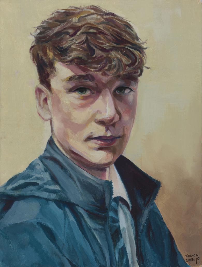 A young man wearing a blue anorak over a white school shirt and tie looks directly at the the viewer.