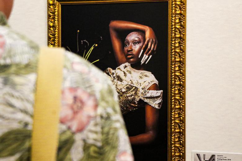Photo, taken over a person's shoulder, of a gilt-framed photograph of a model.