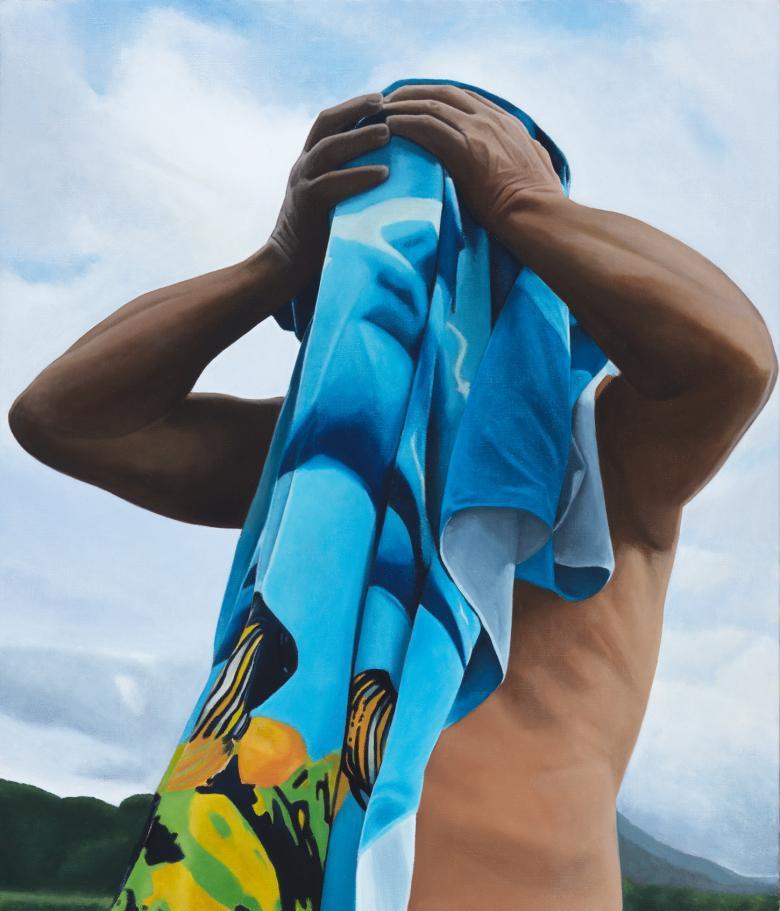 A figure holds a blue and yellow beach towel up to their face, apparently drying after a swim. Behind, we see blue cloudy skies, and green hills.