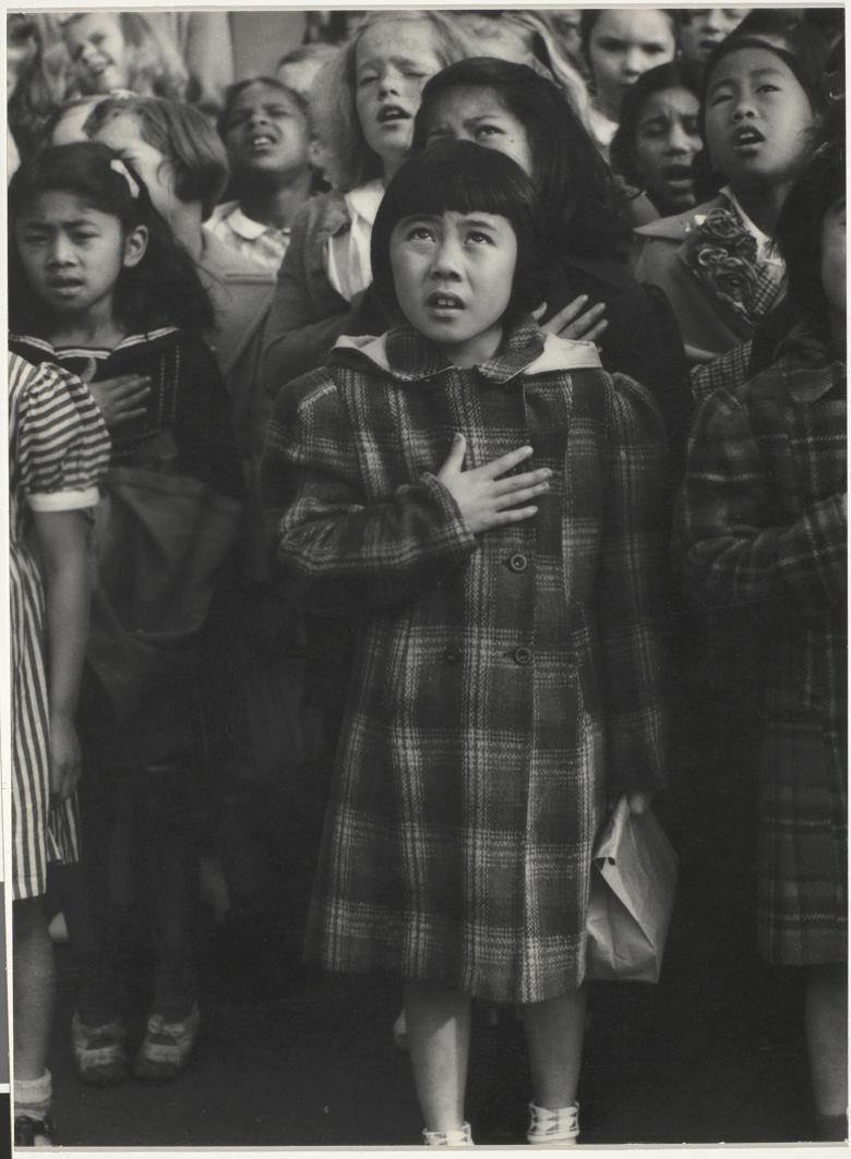 Black and white photo of children standing with one hand on their chests, pledging allegiance.