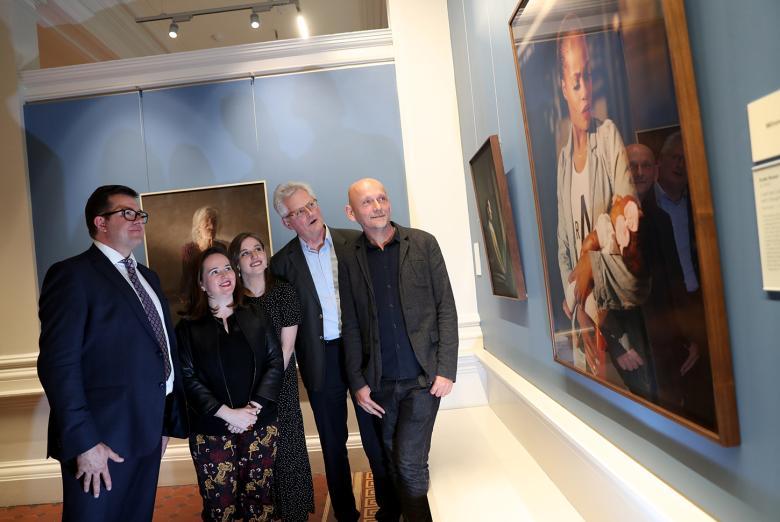 Photo of two women and three men looking at a portrait in a gallery