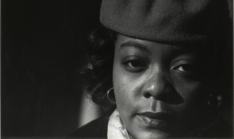 Black and white closely cropped photographic portrait of a woman wearing a hat
