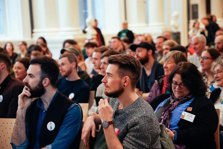 A rapt audience looks towards a point off camera.