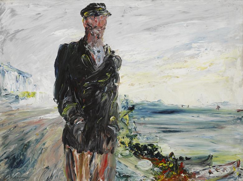 A man in a dark overcoat with his hands in his pockets, wearing a cap. In the background, the sea.  