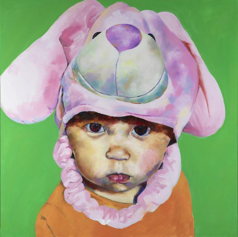 A toddler stares solemnly at the viewer, wearing a hat of a soft toy's head. He stands in front of a vibrant green background, and wears an orange vest.