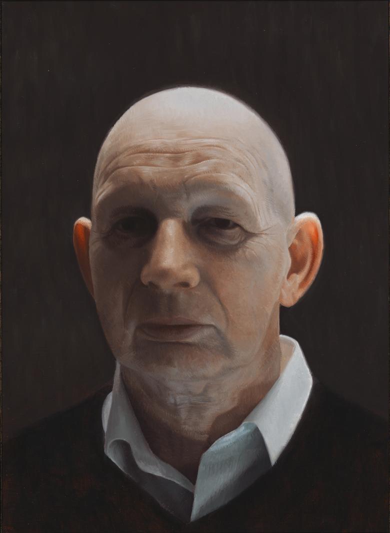 A man stands in shadow. We see his head - he wears a white collared shirt and a dark v-neck jumper.