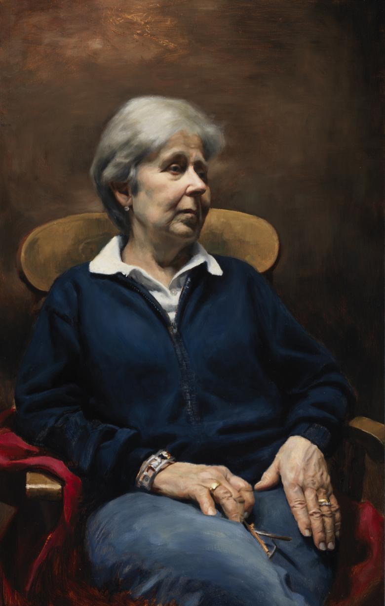 A woman sits in a chair, looking to the right of the frame. Her hands are in her lap.