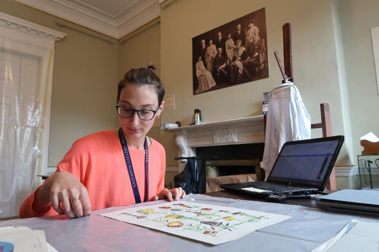 Paper conservator Mathilde Renauld sits at a table, working on a work on paper.