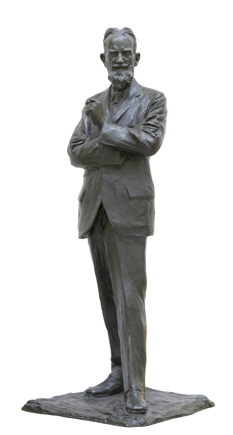 Bronze sculpture, 188cm high, of a bearded man wearing a suit, with arms crossed and left slightly raised
