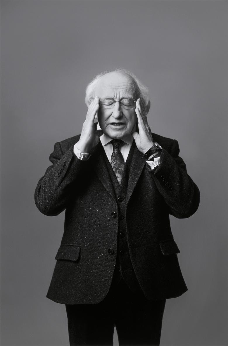 Black and white photograph of man with white hair, balding head and eyes closed, touching his temples