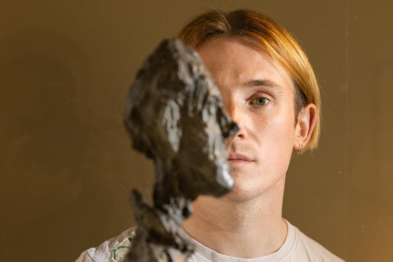 Richard Malone posing behind a bust by Alberto Giacometti
