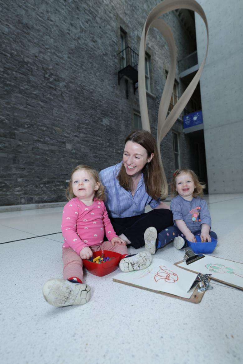 Photograph of a young woman in a blue top with two toddlers