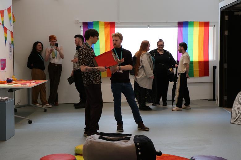 Photograph of a number of young people talking in a small room decorated with rainbow flags and bunting