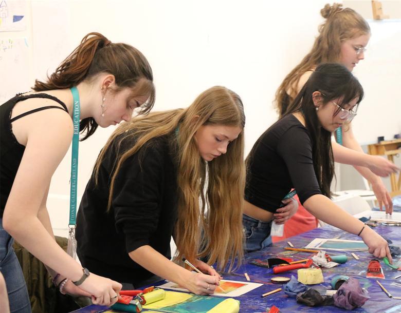 Four girls standing and painting on a purple table.