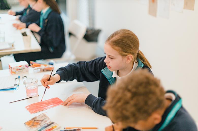 Young girl in a blue school uniform painting at a white table.