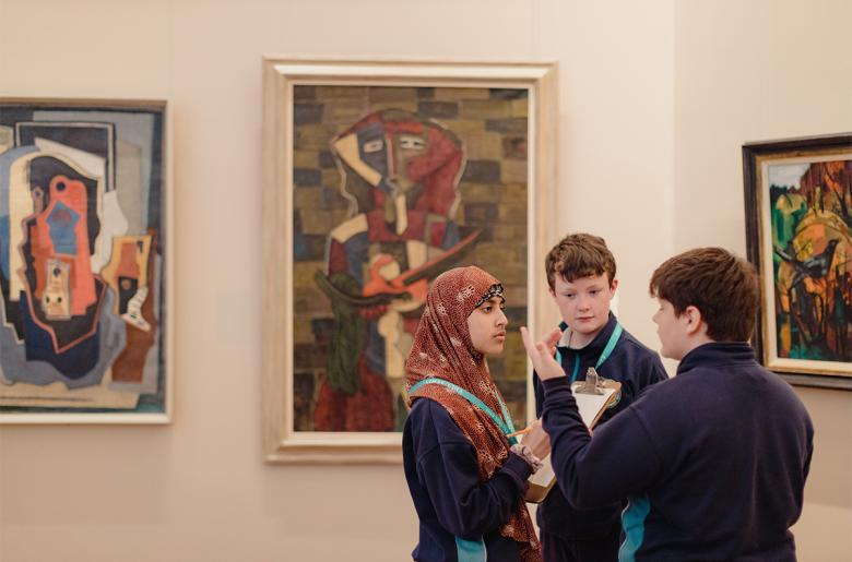 Three children stand together talking in front of three modernist paintings
