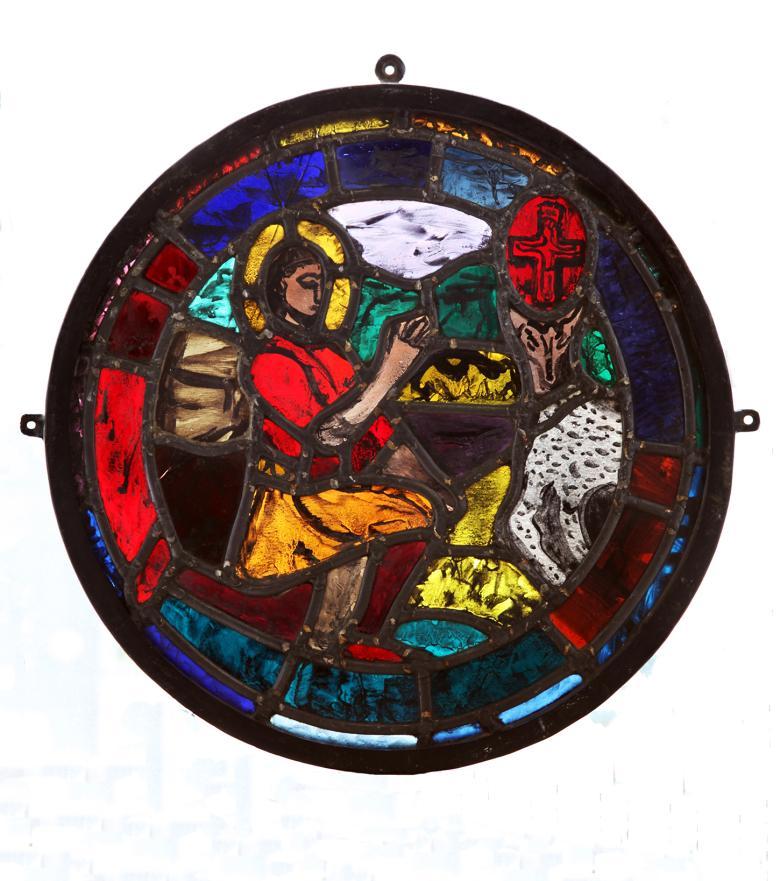 A circular stained glass artwork featuring a figure with his hands in prayer, and a sheep