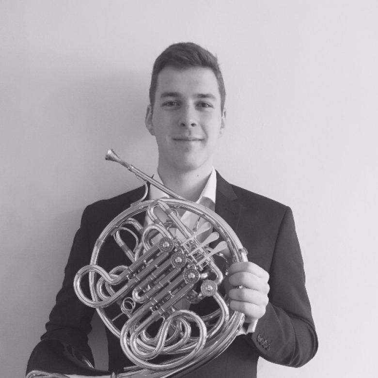 Black and white image of a male figure with short dark hair, holding a French horn