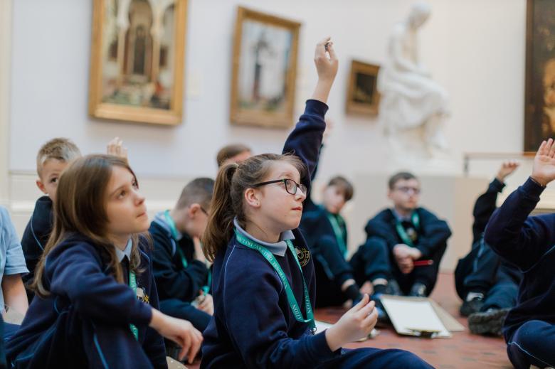 A group of young children in school uniform sit on the floor of an art gallery.