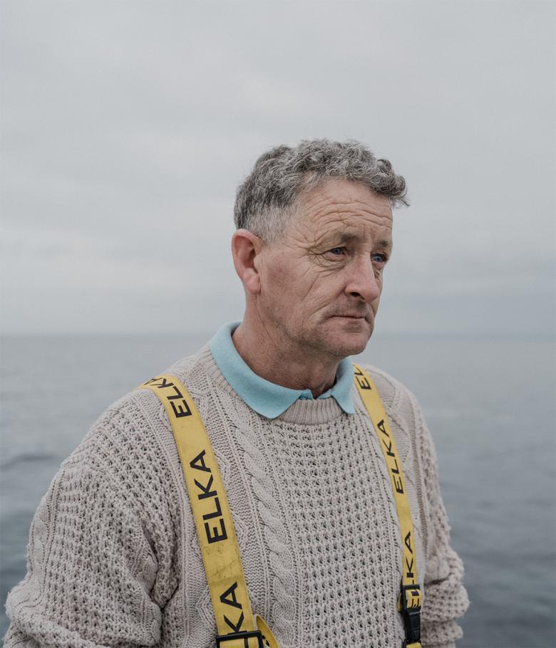 A photograph of a fisherman in a white aran jumper on a boat with a dejected expression