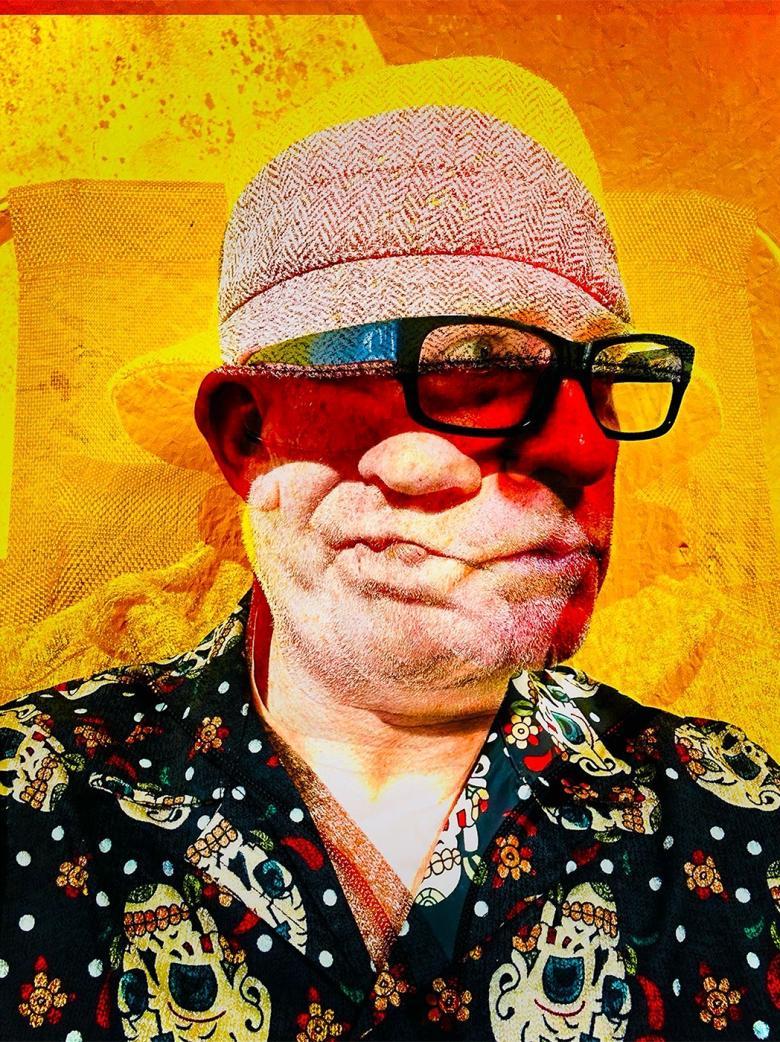 A man wearing a skull print shirt, glasses and a pink hat shakes his head.