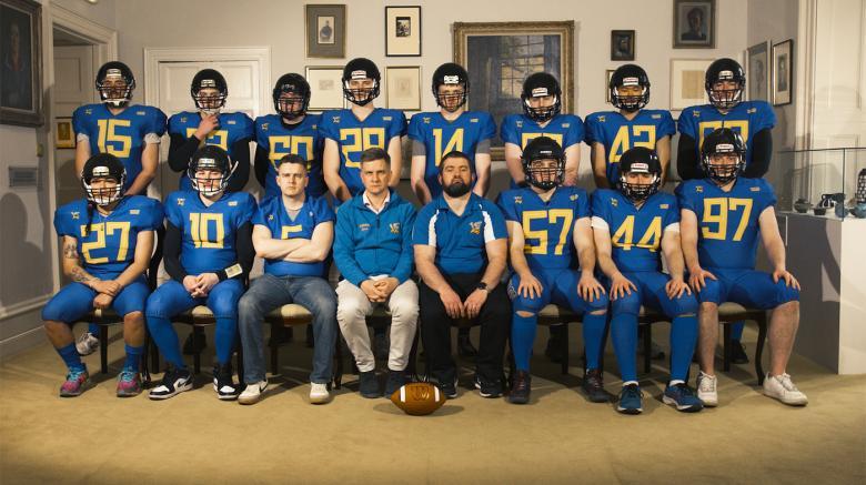 A photograph of an American football team, wearing their helmets and blue jerseys.