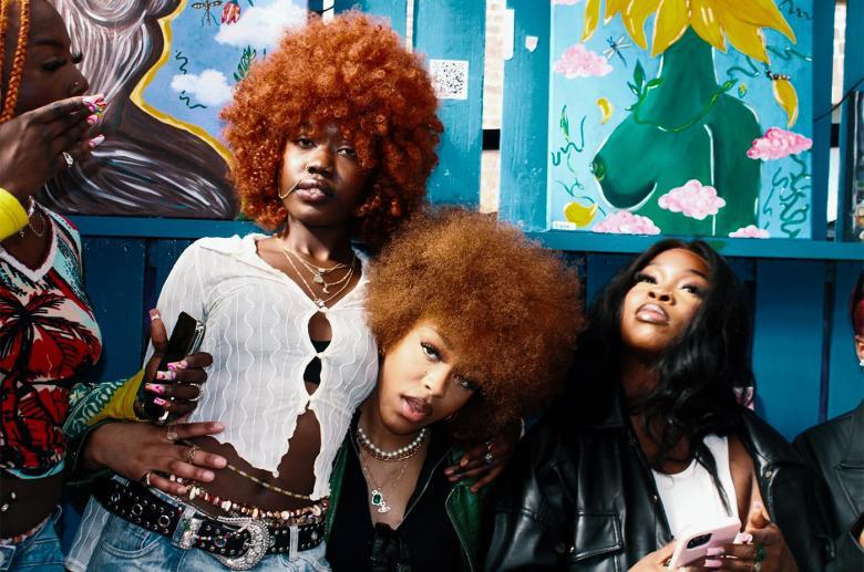 A photograph of four young black women. Two have ginger curly hair and are looking into the camera.