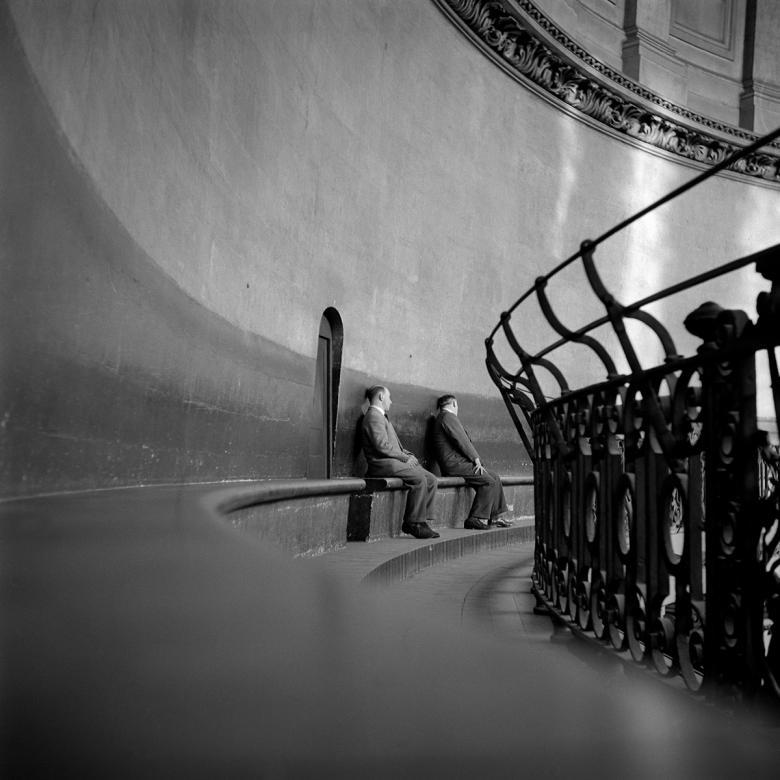 Black and white photograph of two men sitting on a bench within the curved dome of St Paul's Cathedral