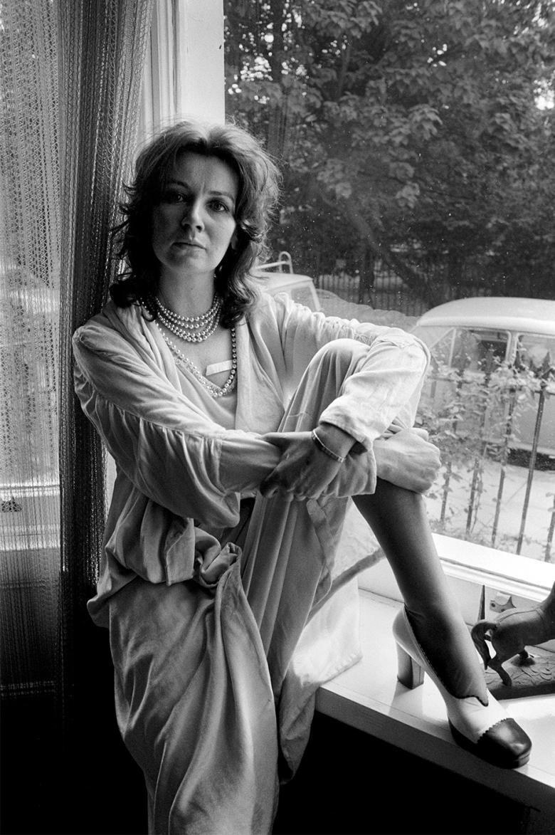 Black and white photograph of a woman sitting with her leg up on a windowsill.