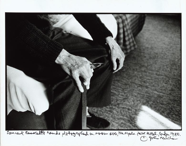Black and white photograph focusing on an older man's hands as he sits on the edge of a bed, resting his hands on his knees