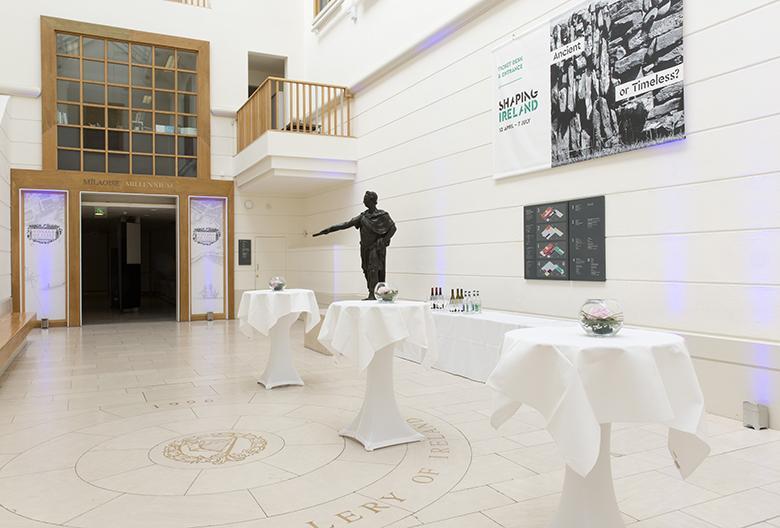 Large white room with high ceilings and tall white tables in front of a bronze statue