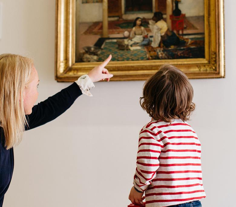A woman crouched down beside a small child and pointing at a painting on a tour of the National Gallery of Ireland.