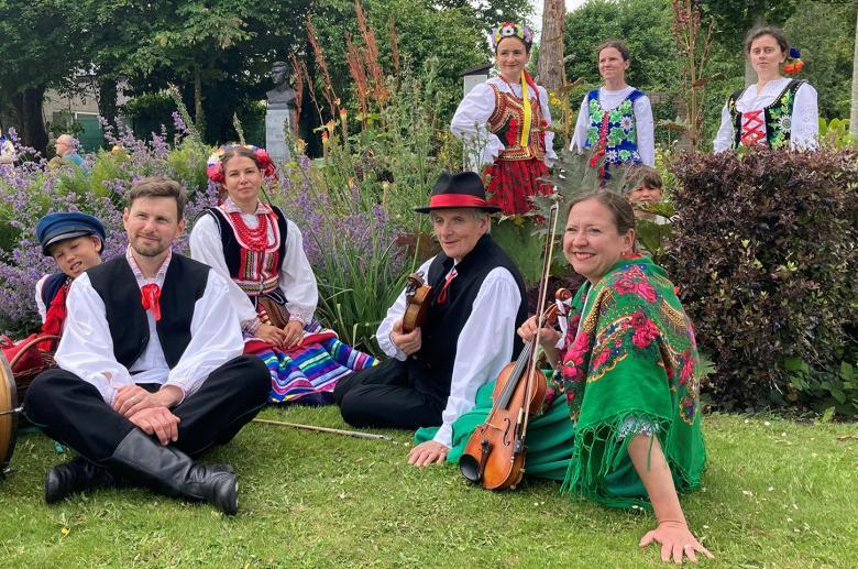 A group of musicians in colourful clothing sit in a park