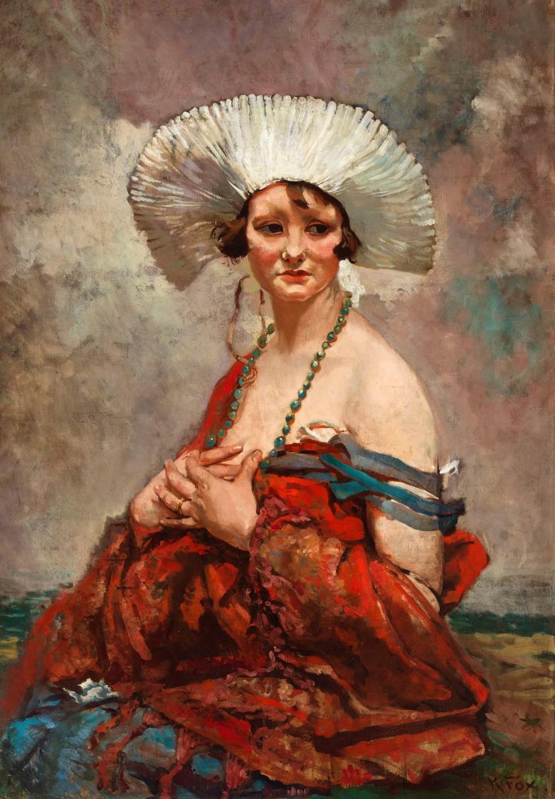 A woman sits wearing a starched white headdress and long beaded necklace. A shawl has fallen off her bare shoulders. 