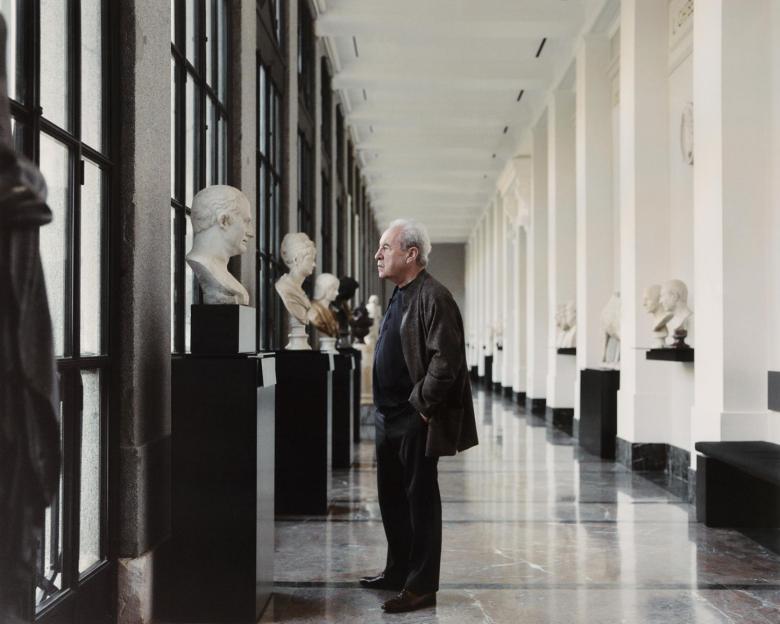 Writer John Banville stands in a corridor of the Prado Museum looking at a row of busts.