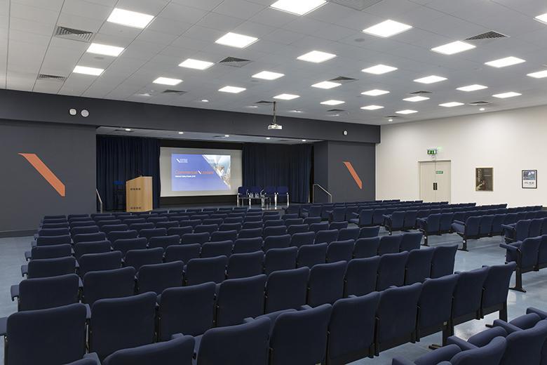 Lecture theatre with rows of dark blue chairs facing a screen