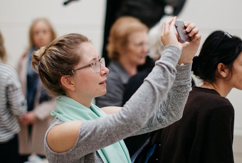 A woman holding up a mobile phone to take a photograph in the Gallery.