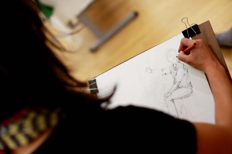 Photo of a woman drawing a human figure on paper.