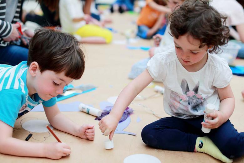 Photo of two children drawing on a giant sheet of brown paper on the floor.